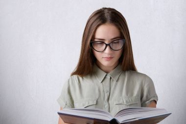 Bir genç kız öğrenci ile uzun düz saç gömlek ve bir kitap okuma şey gözlük takıyor. Beyaz arka plan üzerinde izole ansiklopedi Okuma bir genç kız. Eğitim kavramı.