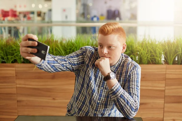 Şık saç kesimi yakışıklı Kızıl saçlı adamla restoranda ciddi ifade çeneme elini tutarak sahip yeşillik içinde izole bir dinlenme yaparken selfie yapım kontrol şık gömlek giymiş — Stok fotoğraf