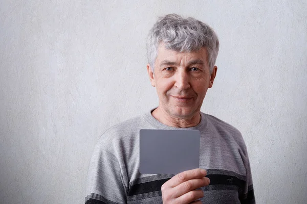 Un retrato horizontal de atractivo hombre maduro con canas y arrugas vestido con suéter casual sosteniendo una tarjeta en blanco con espacio de copia para su texto o contenido publicitario . —  Fotos de Stock