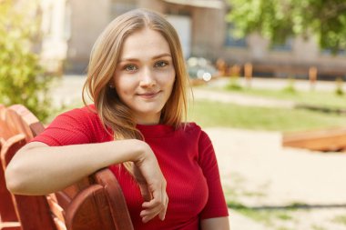 Sevimli sarışın kadın çekici ile gözleri, ince dudaklar ve kırmızı kazaklı açık havada tahta bankta yaz tatil sırasında dinlenme. giyiyor, çilli. İnsanlar, gençlik, tatiller, yaşam tarzı ve dinlenme kavramı