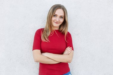 Kendine güvenen kadın kırmızı giysili yüzünde kamera beyaz duvarının yakınında dururken bakarak mavi gözlü, Sarı saçlar ve çiller sahip eller geçti. İnsanlar, gençlik, güzellik, yaşam kavramı