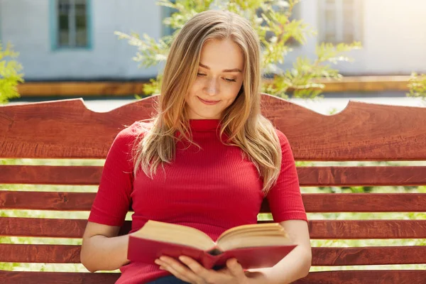 Lidé, hobby, odpočinek koncept. Mladý student krásná žena s rovné blond vlasy a na sobě čisté zdravé kůže, červené oblečení drží knihu s pozorný pohled v něm líbí moc číst — Stock fotografie