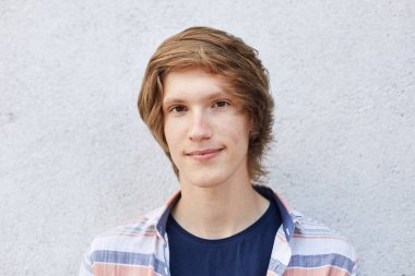 Yakın çekim yakışıklı erkek koyu renk gözleri, saf sağlıklı deri ve ince dudakları ile ciddi ifade doğrudan kameraya bakıyor. Hipster çocuk beyaz duvara poz çekici görünümü ile