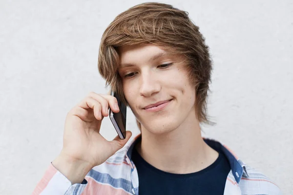 Close up portrait of handsome young boy with narrow dark eyes, stylish hairdo, dimple on cheek holding his mobile phone on ear calling somebody. People, youth, modern techologies and lifestyle — Stock Photo, Image
