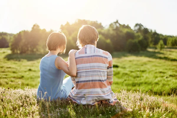 Vue arrière d'adolescent romantique garçon et fille assis ensemble à l'herbe verte embrassant avoir parler reposant ayant de bonnes relations et la compréhension. Les gens, l'unité et le concept de romance — Photo