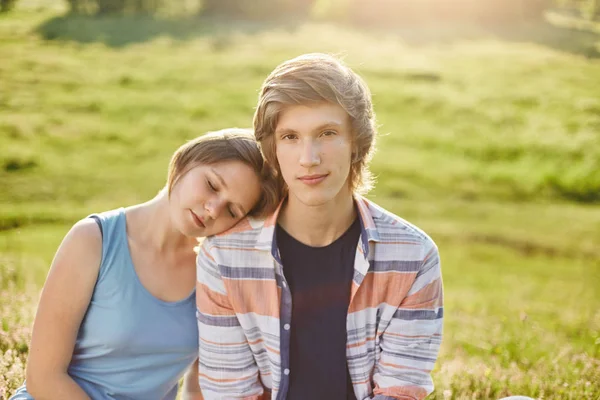 Jolie fille penchée à l'épaule de son petit ami fermant les yeux avec plaisir profiter ensemble atmosphère calme tout en étant assis à l'extérieur à l'herbe verte. Couple romantique amoureux reposant sur le terrain — Photo