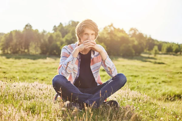 Nadenkend tiener zitten buiten op het veld bewonderen pittoreske landschappen na te denken over iets met ernstige expressie. Aantrekkelijke jongen buiten ontspannen. Mensen, lifestyle, natuur, ontspanning — Stockfoto