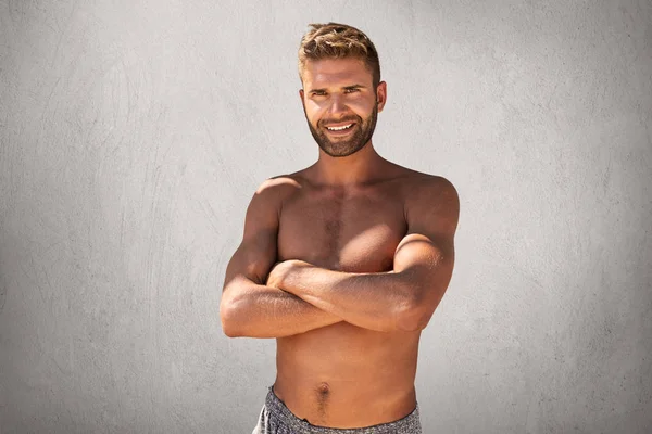 Portrait taille haute d'homme attrayant musclé à la coiffure et aux poils à la mode, en gardant les mains croisées sur fond gris crème isolé. Fort beau mâle souriant à la caméra tout en étant nu — Photo