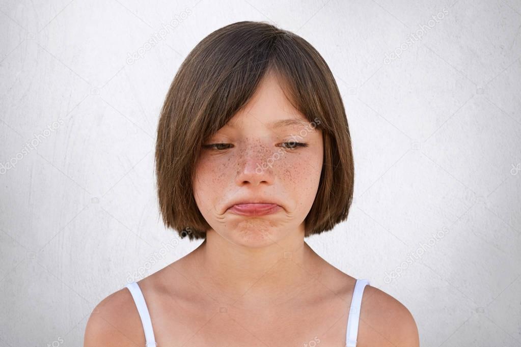 Little upset girl with freckled skin and bobbed hair, curving her lips with sorrorful expression being unhappy to find out that parents didn`t buy her toy. Freckled beautiful girl going to cry