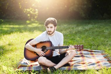 Duygu zevk ve gevşeme güneşli hava ve güzel manzaralar, onun bağdaş tutmak zevk gitar ile yorgan üzerinde oturan yazlık giysiler giyen yakışıklı sakallı adam. Erkek gitarist