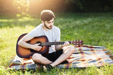 Oturup gitar ile çekici şık sakallı adamın portre sakin atmosferi tadını müzik aleti çalma yeşil çimenlerin üzerinde bacak bacak. Yetenekli çocuk dinlenme sırasında onun yetenek gösteren