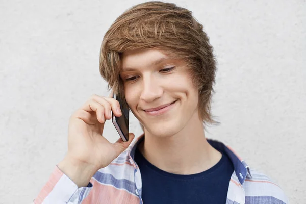 Portré, szép tizenéves fiú, divatos frizura, mosolyogva, óvatosan, hogy közelről gödröcske az arca, a hívás a legjobb barátja, mint szúró telefon, intézi a vele. Technológia, életmód — Stock Fotó