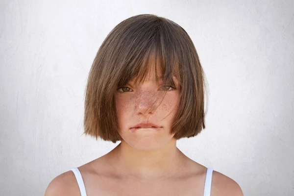 Niña molesta peleando con sus padres, mirando inocentemente a la cámara mientras curva sus labios aislados sobre un fondo blanco. Niña triste llorando, mordiéndose el labio inferior —  Fotos de Stock