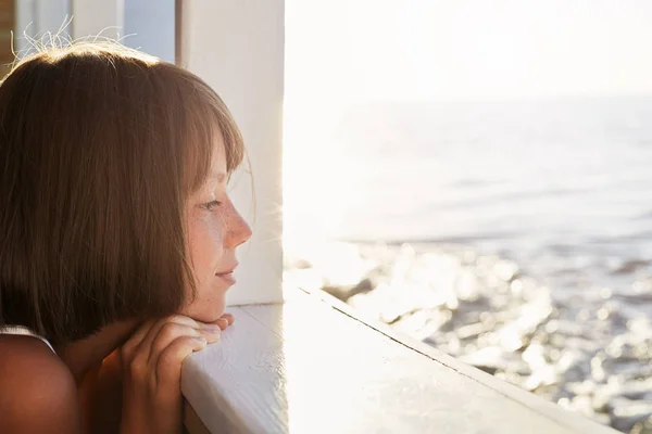 Little child with short dark hair, looking out from deck of ship, admiring calm sea while resting during her summer holidays. Beautiful girl having sea voyage on yacht looking at sea with dreams — Stock Photo, Image