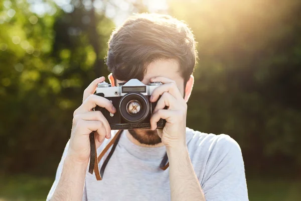 Young creative photographer making photos with retro camera, photographing beautiful landscapes of nature while resting at green field. Male using vintage retro film camera at green summer field — Stock Photo, Image
