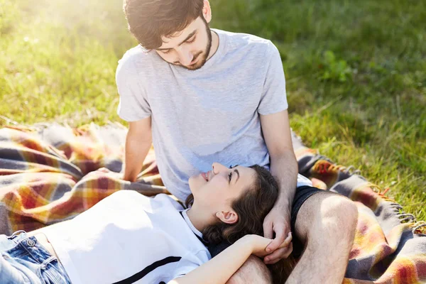 Vacances, vacances, amour et amitié concept. Couple amoureux reposant ensemble sur l'herbe verte de prairie, se regardant dans les yeux avec un grand amour. Femme couchée sur les genoux de son petit ami et se reposant — Photo