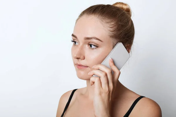 Gros plan portrait de femme blonde regardant de côté avec une expression sérieuse tout en appelant son ami ou sa famille, écoutant attentivement quelque chose. Jeune fille attrayante bavarder sur téléphone mobile . — Photo