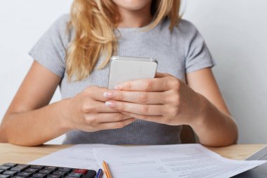 Genç kadın girişimci gri T-shirt, akıllı telefon kağıt iş vasıl yazıhane sonra dakika istirahat elinde tutarak, görüntüsünü kırpılmış. Dalga köpüğü enterne iş günü içinde cep telefonundan işkadını