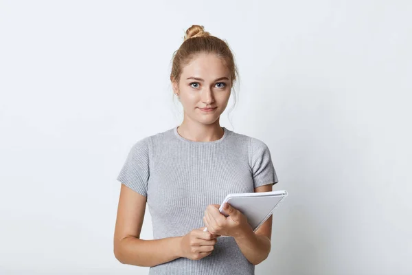 Portrait of female student with light hair bun, dressed casually, keeping notebook in hands, going to write notes of lecture, isolated over white background. Woman with pocketbook posing in studio — Stock Photo, Image