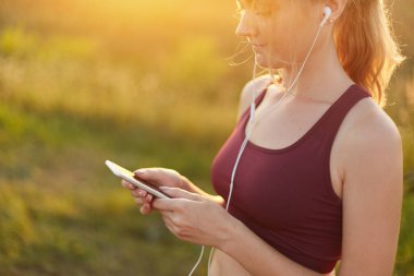 Temiz hava ve güneş keyfi kulaklık ve cep telefonu, müzik dinlerken koşma, spor, giyen üst yapıyor sportif kadın. Modern cep telefonu kullanarak ince kadın atlet. Spor kavramı