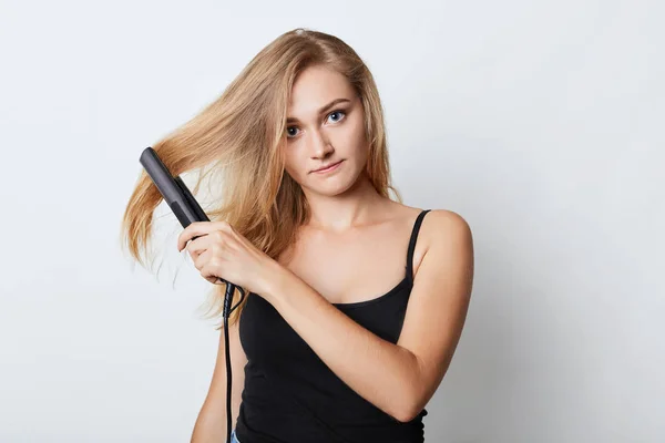 Fashion hairstyle concept. Beauiful female with long hair, straightens it with hair iron. Woman after taking shower does hairstyle as going on work, isolated over white background. Hairdressing — Stockfoto