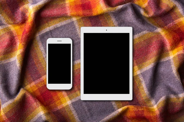 Moredn devices on warm colorful coverlet: digital tablet and smart phone with blank screens. Domestic atmosphere. Unrecognizable person spends free time at bed, uses gadgets — Stock Photo, Image