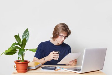 Konsantre işadamı içinde gözlük sınavları yakından kağıt, içecekler paket kahve, mali değerlendirmeleri, önünde açılan dizüstü oturur. Ciddi adam elinde belge okur, her şeyi analiz eder