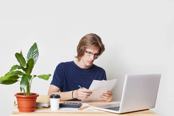 男性的营销专家用心读合同、 研究图表和图形，有手提电脑在家里工作，孤立在白色工作室的背景。专业年轻上班族在室内 — 图库照片
