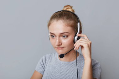 Ciddi kadın yardım hattı operatörü gri arka plan üzerinde izole bir şey odaklı onun iş için kulaklık kullanır. İşkadını ortakları telefonları. İş, çağrı merkezi ve teknoloji kavramı
