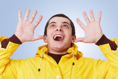 Neşeli gülümseyen heyecan brunet adam sarı anorak hareketleri aktif giyer, mutlu görünüyor, tavanda, hoş bir şey kopya alanı metni ile mavi arka plan üzerinde izole fark.