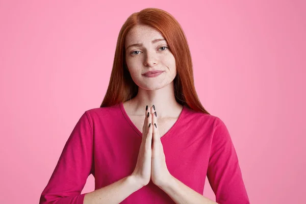 Portrait horizontal de jeune femme européenne avec taches de rousseur presse les paumes ensemble en geste de prière, supplie quelque chose dont elle a grandement besoin, isolé sur fond rose. Femme demande pardon — Photo