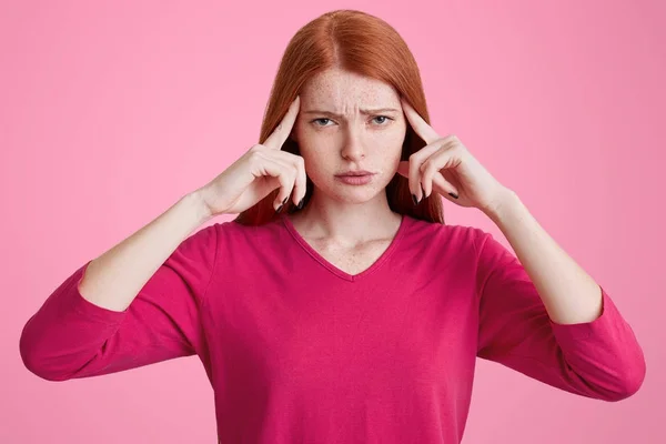 Frustrasi perempuan dengan bintik-bintik kulit, rambut merah lurus, menjaga jari-jari di kuil, tampak bingung pada kamera, memiliki pandangan yang tidak bahagia, mencoba untuk berkonsentrasi pada sesuatu, memiliki sakit kepala dan banyak masalah — Stok Foto