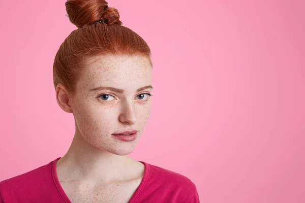 Крупним планом портрет веснянки-жінки з пучком імбирного волосся, носить рожевий светр, впевнено дивиться в камеру, думає про майбутні плани, позує в приміщенні. Приваблива руда жінка в студії — стокове фото