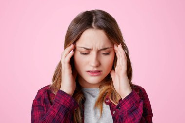 Yorgunluk overworked stresli kadın modeli tapınak üzerine ellerini tutar, korkunç baş ağrısı muzdarip, gözlerini kapatır, ağrı hissediyor, pembe arka plan izole rahat kareli gömlek giyer. Yorgunluk cocnept