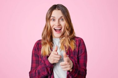 Heyecanlı çok memnun kadın modeli düz saçlar, koyu renk gözleri, saf deri ile sevinç içinde ağız açılır ve wih ön plana sen gösterir parmak pembe arka plan üzerinde izole bir şey seçmek memnun olmak,