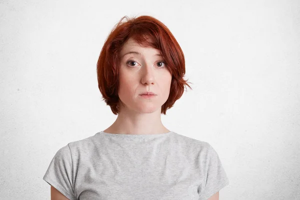 Πορτρέτο του σοβαρές Κοκκινομάλλης γυναίκα φοράει casual t πουκάμισο ακούει προσεκτικά συνομιλητή, προσπαθεί καταλάβει πληροφορίες, απομονωμένη κατά τη διάρκεια συγκεκριμένων λευκό φόντο. Φωτογραφία μόδας τζίντζερ γυναίκας — Φωτογραφία Αρχείου