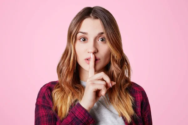 Hermosa joven hembra con apariencia atractiva mantiene el dedo en los labios, muestra signo de silencio, pide estar tranquilo, aislado sobre fondo de estudio rosa. Un gesto de silencio. Mujer gestos interior — Foto de Stock