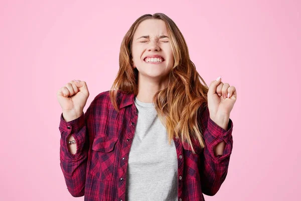 Ευρωπαϊκό περιχαρής νικητή ευτυχισμένη γυναίκα με ευχάριστο χαμόγελο, σφίγγει τις γροθιές και τα δόντια, χαίρεται την νίκη ή επίτευξη μεγάλη επιτυχία, απομονώνονται σε ροζ φόντο. Τυχερή γυναίκα δημιουργεί εσωτερική — Φωτογραφία Αρχείου