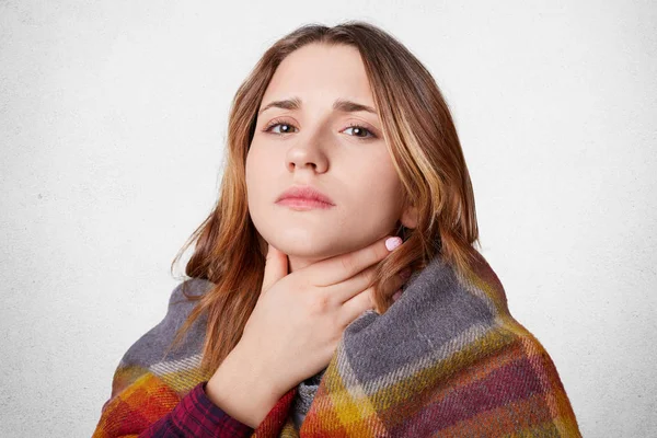 Mujer disgustada cubierta con manta caliente, tiene garganta profunda, no puede decir ninguna palabra, mira con mala expresión infeliz, aislado sobre fondo blanco. Invierno, enfermedad, personas, concepto de tratamiento — Foto de Stock