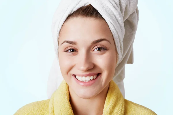 Beautiful female with cheerful smile, wears towel and bathrobe, has healthy pure skin, looks happily into camera, isolated over white background. Woman in dressing gown. Clean face and healthy skin — Stock Photo, Image