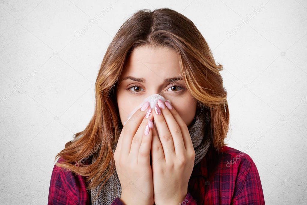 Close up portrait of beautiful woman sneezes and coughs, uses tissue, rubs nose, has bad cold, isolated over white background. Low spirited desperate woman suffers from cold and running nose