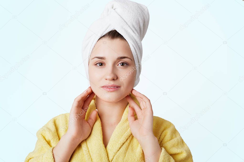 Adorable young lovely woman in bathrobe and towel, has shower, poses against white background, being glad spend time at home, has spa procedure. People, hygiene, beauty and healthcare concept