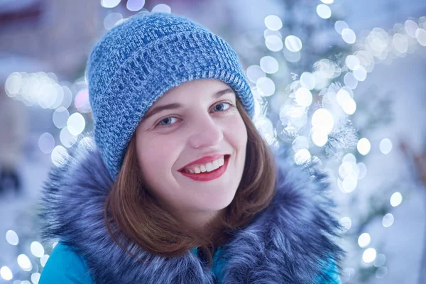 Portret van aangenaam uitziende jonge vrouw met blauwe ogen, rode lippen, gezonde huid, close-up draagt warme gebreide muts en jas, besteedt tijd buiten tijdens de wintervakantie, blij om te poseren op camera Rechtenvrije Stockfoto's