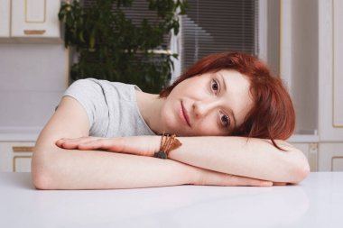 Kırmızı saçlı güzel kadın modeli portresi boyuyla eğilir, ev, kayıtsızca, giyinmiş hakkında sıkı çalışma hafta sonları evde geçirir sonra bitkin görünüyor, mutfak iç oturur. Aile içi atmosfer