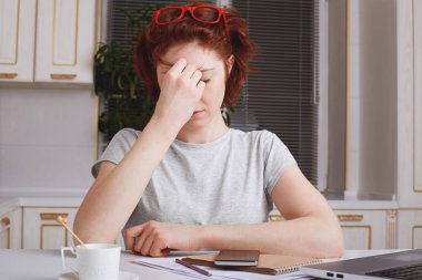 Stresli yorgunluk kağıtları ve modern teknolojiler ile çevrili genç erkek aşırı konsantre olmaya çalışır mutfak iç oturur. Hayal kırıklığına uğramış yorgun Kızıl saçlı öğrenci baş ağrısı vardır