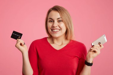 Mutlu kadın modeli maaş almak için bayram yapıyor, tutan plastik kart ve denge doğrulamak için modern akıllı telefon, mobil bankacılık uygulaması, evde alışveriş online yapacak kullanır. Online ödeme