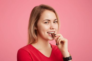 Memnun içerik erkek ısırıkları lezzetli tatlı çikolata, onun tadı sahiptir, ifade ve hoş bak, tatlı, pembe bir arka plan üzerinde izole yemek memnun görünüyor doğrudan kameraya mutlu vardır