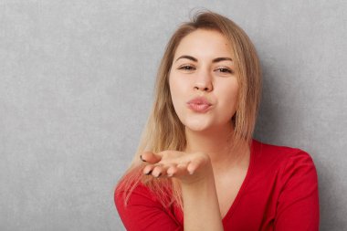 Yatay atış ile görünüm, çekici güzel ve genç birbayan öpücük, darbeler kamera hava yapar, kopya alanı Promosyon metni ile gri bckground üzerinde izole kırmızı Kazak giyer