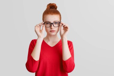 Kırmızı saç düğüm ile kendine güvenen kız öğrenci gözlük ciddi ifade ile bakar, beyaz arka plan üzerinde izole dikkatle, ders dinler. Kavram okuyan insanlar, güzellik,