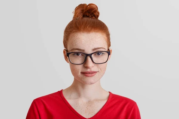 Close up retrato de sardento muito jovem fêmea usa óculos quadrados, camisola vermelha, pensa em algo, tem expressão agradada, isolado sobre fundo branco. Conceito de beleza e estilo — Fotografia de Stock